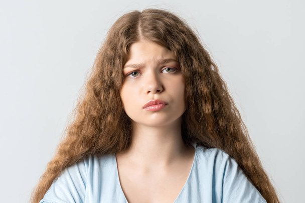 Offended pensive girl with curly long hair posing isolated on white background. People lifestyle concept. Holding hands crossed, looking at camera. - Photo, Image
