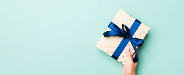 Les mains de femme donnent Noël enveloppé ou autre cadeau fait à la main de vacances en papier coloré. Coffret cadeau, décoration de cadeau sur table bleue, vue du dessus avec espace de copie. - Photo, image