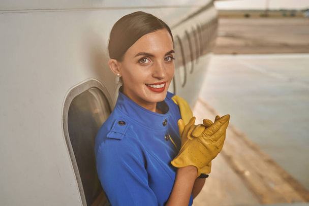Hübsche Flugbegleiterin legt Hände zusammen und lächelt fröhlich - Foto, Bild