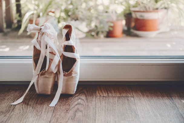 Balett pointe cipő rózsaszín selyem szalaggal az ablak mellett. Régi pointe cipő szatén szalaggal - Fotó, kép