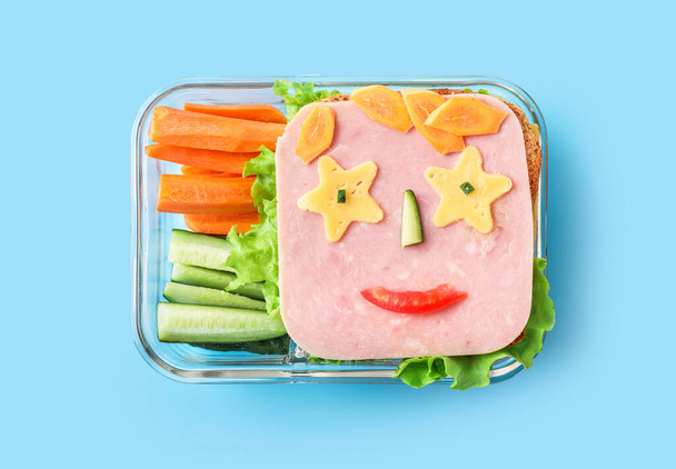 青い背景に面白いサンドイッチと健康的な学校のランチボックス。トップ表示. - 写真・画像