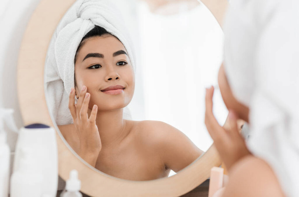 Allegro asiatico giovane donna applicando crema per il viso - Foto, immagini