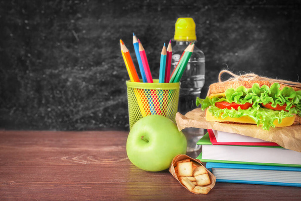 Υγιές σχολικό γεύμα και σχολικά χαρτικά σε ξύλινο γραφείο πάνω από μαύρο φόντο πίνακα. Αντιγραφή χώρου. - Φωτογραφία, εικόνα