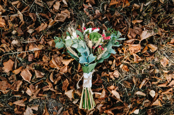 Autumn bridal bouquet of yellow and orange flowers, red berries lying on the grass in fall leaves. Wedding, composition, design, gold autumn. flat lay. top view. - Foto, Imagen