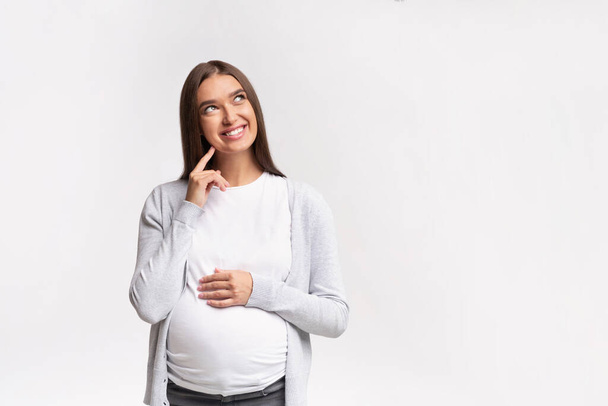 Cheerful Mother-To-Be Dreaming Standing Over White Background In Studio - Photo, image