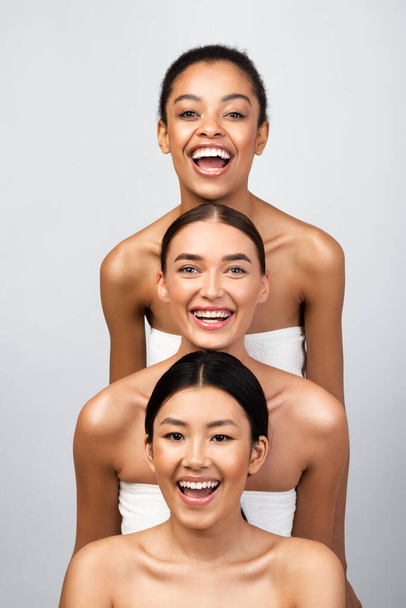 Fröhlich Gemischte Mädchen posieren eingewickelt in Badetücher, grauer Hintergrund - Foto, Bild