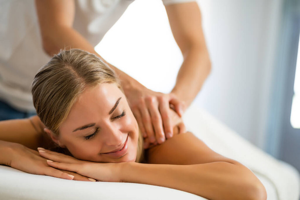 Profesionální masér provádějící terapeutickou masáž. Žena si užívá masáže ve svém domě. Mladá žena dostává relaxační masáž těla. - Fotografie, Obrázek