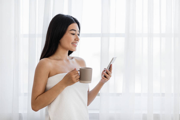 Bonita mujer asiática usando smartphone y bebiendo café - Foto, imagen