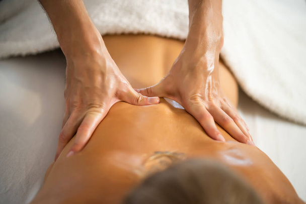 Profesjonalny masażysta robi terapeutyczny masaż. Kobieta lubiąca masaże w domu. Młoda kobieta dostaje relaksujący masaż ciała. - Zdjęcie, obraz