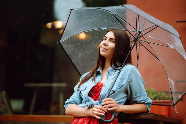 Cheerful woman holding umbrella while strolling outside. Beautiful woman with umbrella on a rainy day on the street. Autumn concept. - Zdjęcie, obraz