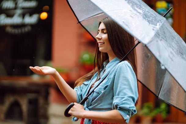 Cheerful woman holding umbrella while strolling outside. Beautiful woman with umbrella on a rainy day on the street. Autumn concept. - Фото, зображення