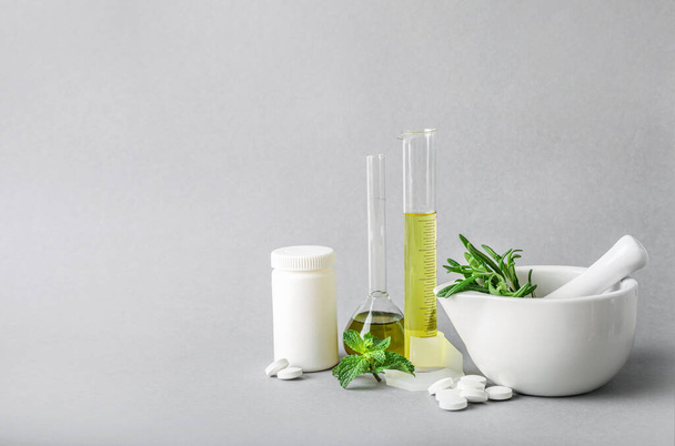 Mortar with pestle, laboratory glass equipment with natural ingredients and herbal pills on grey background. Copy space. Herbal medicine concept. - Фото, изображение