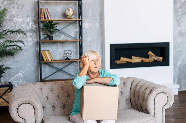 Senior woman is unpacking a cardboard box - Zdjęcie, obraz
