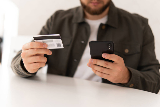 Comprar en línea con una tarjeta de crédito y un teléfono inteligente sentado en casa con un fondo borroso. tarjeta de crédito de mano para compras en línea. Compras web. pago compras en línea smartphone en el lugar de trabajo. - Foto, imagen