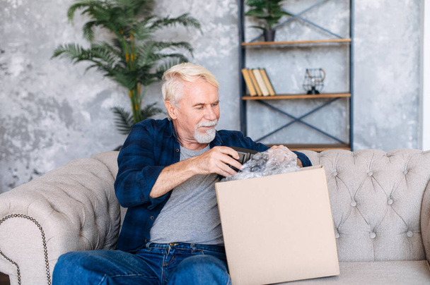 Mature man unpacking a cardboard shipping box - Foto, afbeelding