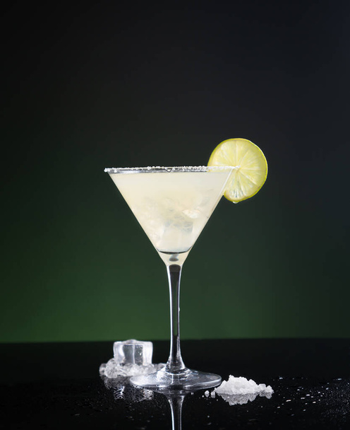 Typical Mexican margarita cocktail with lime slice and ice on black and green background. - Fotografie, Obrázek
