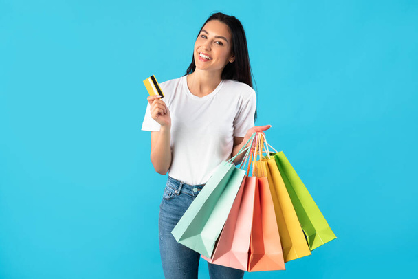 Kredi kartı tutan ve alışveriş torbaları taşıyan bir kadın. - Fotoğraf, Görsel