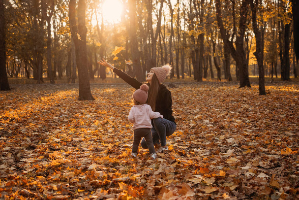 Happy family mom and baby girl playing outdoors in fall park. Little girl and her mother in the autumn park. - Photo, Image