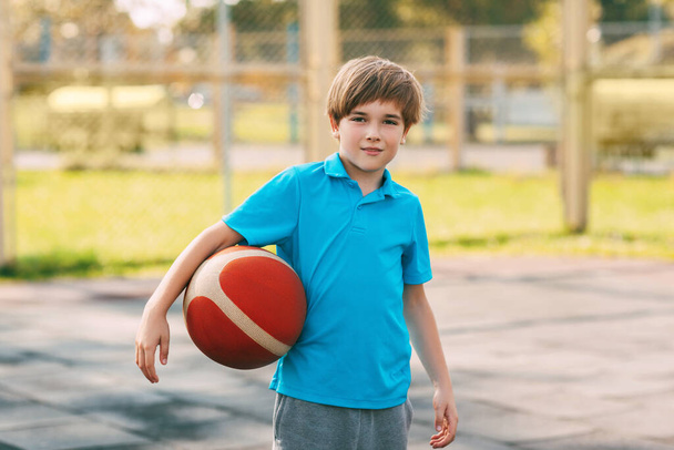 バスケットボールを手にしたスポーツ制服を着た笑顔の少年の肖像画。少年はバスケットボールをした後ボールを手に持っている。. - 写真・画像