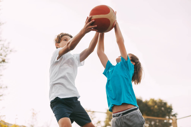Dwóch nastolatków gra w koszykówkę na placu zabaw. Sportowcy walczą o piłkę w grze. Zdrowy styl życia, sport - Zdjęcie, obraz