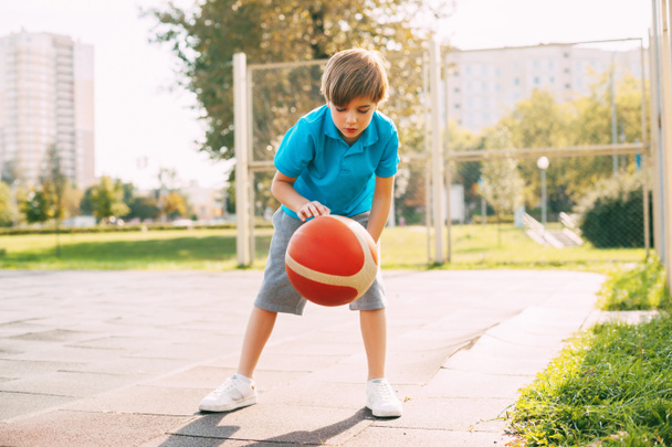 Odaklanmış yakışıklı sporcu çocuk basketbol maçında topa öncülük ediyor. Okuldan sonra basketbol oynayan bir çocuk.. - Fotoğraf, Görsel