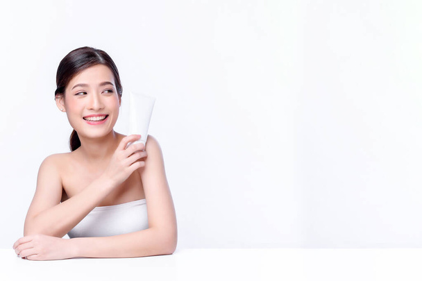 Portrait de belle charmante jeune femme asiatique posant faciale avec cosmétique et assise avec table blanche, beauté du visage féminin avec soins de la peau sur fond blanc, concept de soins de santé et de soins de la peau.  - Photo, image