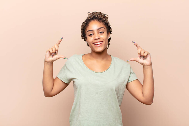 young afro woman framing or outlining own smile with both hands, looking positive and happy, wellness concept - Photo, Image