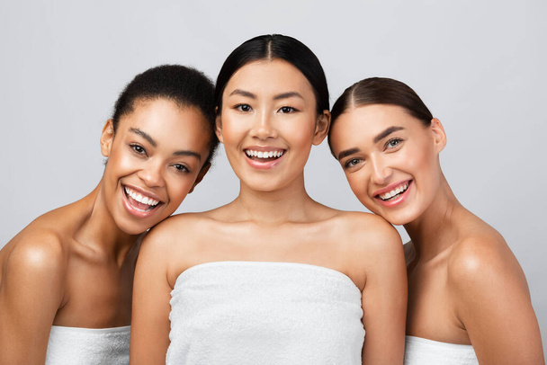 Три молодые женщины смеются, завернутые в полотенца, серый фон - Фото, изображение