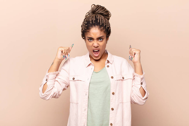 young afro woman shouting aggressively with an angry expression or with fists clenched celebrating success - Foto, Imagen