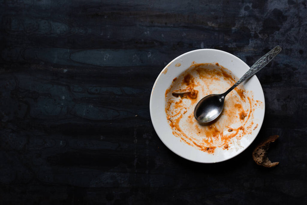 on a dark metal plate, an empty white plate with a spoon, stained after eating - 写真・画像