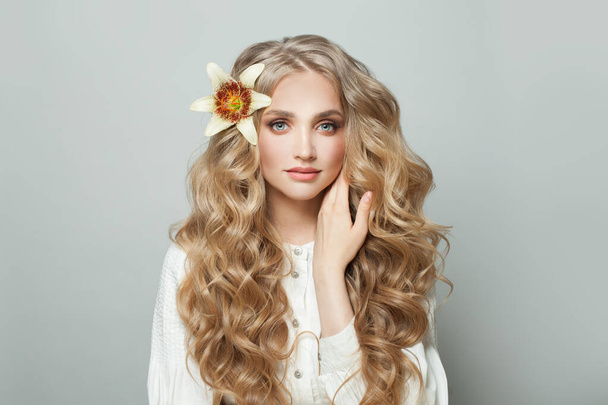 Mulher loira bonita com flor no cabelo encaracolado longo no fundo branco - Foto, Imagem