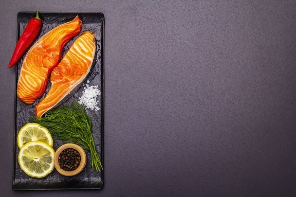 Nyers norvég pisztráng. Egy darab friss hal, citrom, kapor, csípős bors, só. Sushi minőségű, fekete kő beton háttér - Fotó, kép