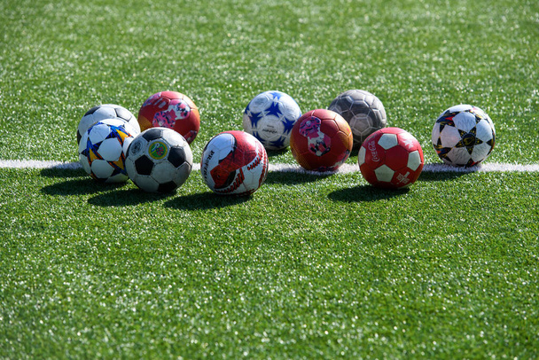 A variety of soccer balls lie on the green lawn of the football field in front of the goal. Ukraine, September 2020. High quality photo - Photo, Image