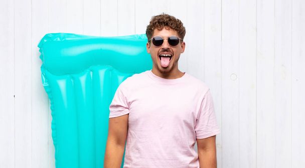 young man with cheerful, carefree, rebellious attitude, joking and sticking tongue out, having fun. holidays concept - Photo, Image