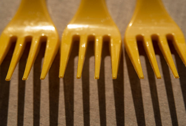 Bright yellow plastic forks on cardboard casts a shadow - Photo, Image
