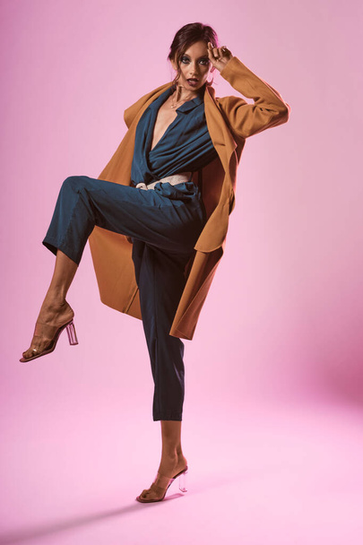 Fashion portrait of a skinny woman wearing a green dress and a yellow coat on a pink background - Photo, Image