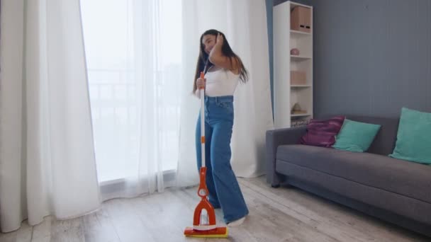 Giovane donna caucasica positiva divertente ballare durante la pulizia della casa - Filmati, video