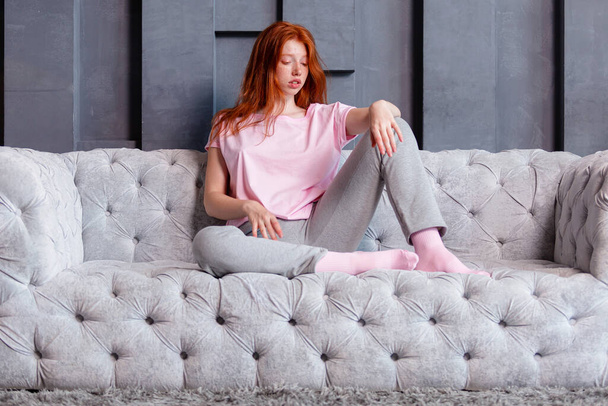 Pretty redhead woman sitting on couch at home and looking in the camera - Foto, Imagem