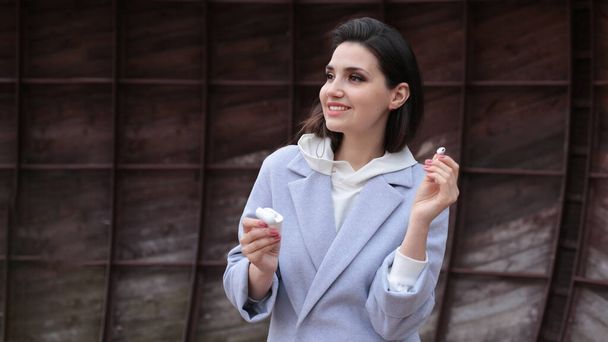 Egy fiatal nő portréja, sötét csíkokkal, fehér kapucnis pulcsiban, vezeték nélküli fülhallgatóval. - Fotó, kép