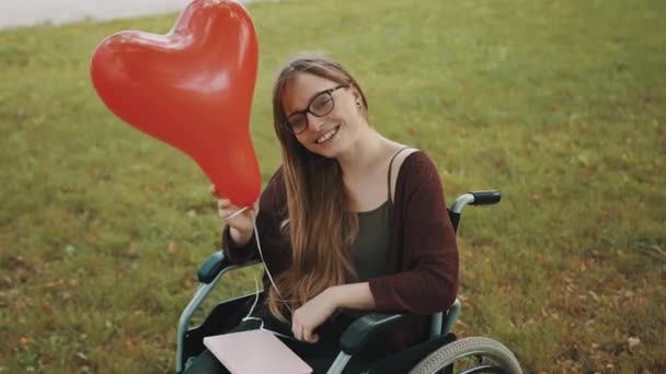 Behinderte junge Frau mit rotem Luftballon hat Spaß in der Natur - Filmmaterial, Video