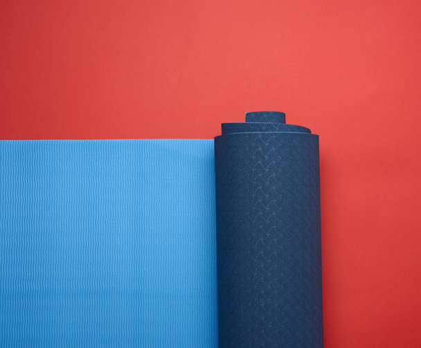 neopreen blauwe gedraaide mat ligt op een rode achtergrond, sportuitrusting, kopieerruimte - Foto, afbeelding