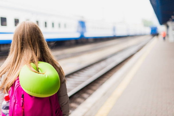 A lány a vonatra vár. Lány hátizsákkal és zöld nyakú párnával - Fotó, kép