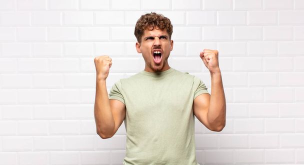 young man shouting aggressively with an angry expression or with fists clenched celebrating success - 写真・画像