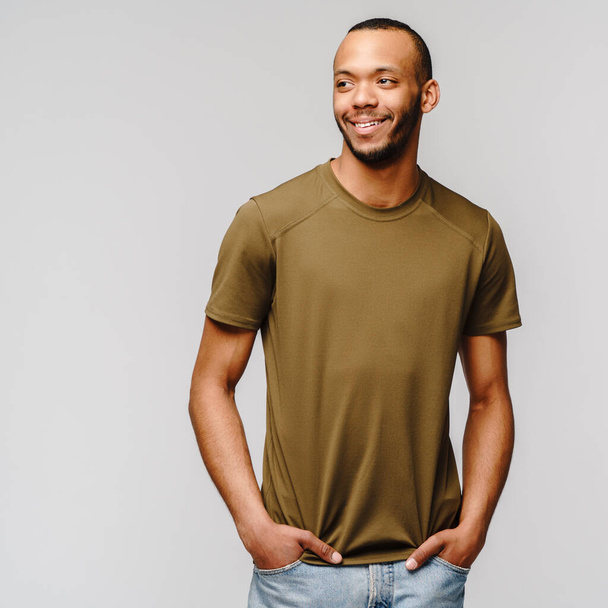 Joyful friendly african-american young man in green t-shirt over light grey background with copy space - Foto, immagini