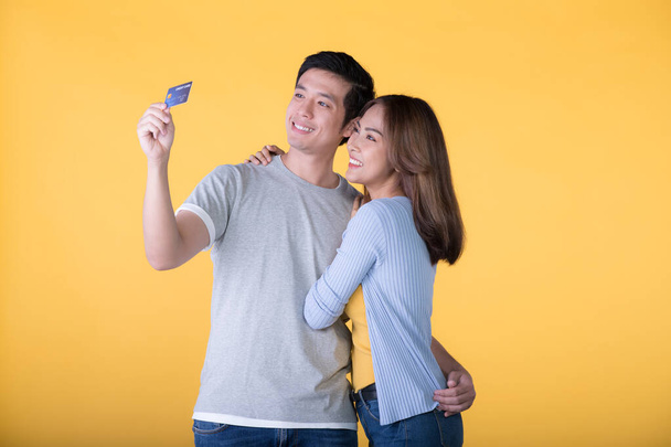 Young Asian couple with credit card isolated on yellow background - Foto, afbeelding