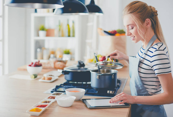 Young woman using a tablet computer to cook in her kitchen - Foto, Bild
