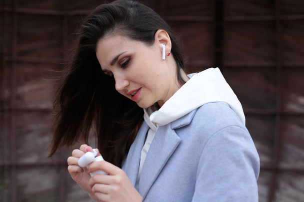 Retrato de una joven con rayas oscuras en una sudadera con capucha blanca con auriculares inalámbricos - Foto, Imagen