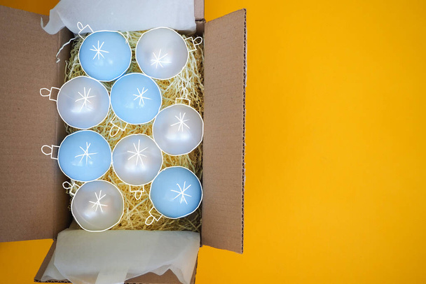 Різдвяні кульки у відкритій картонній коробці жовтий фон. Мистецький колаж
.  - Фото, зображення