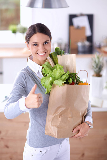 Young woman holding grocery shopping bag with vegetables .Standing in the kitchen - Φωτογραφία, εικόνα