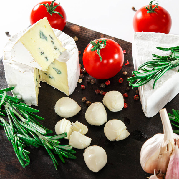 Cheese set. Cheese assorted with vegetables and rosemary lie on a dark board - Photo, Image